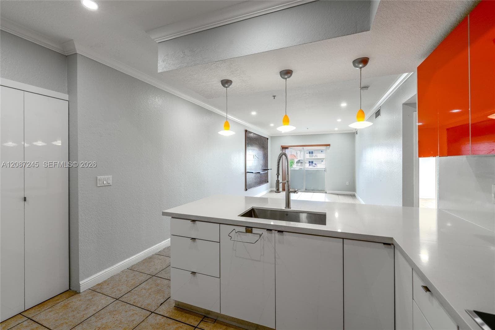 Kitchen featuring high-gloss orange upper cabinetry, white flat-panel lower cabinetry, solid-surface countertops, an undermount stainless steel sink with a pull-down faucet, and a trio of pendant lights