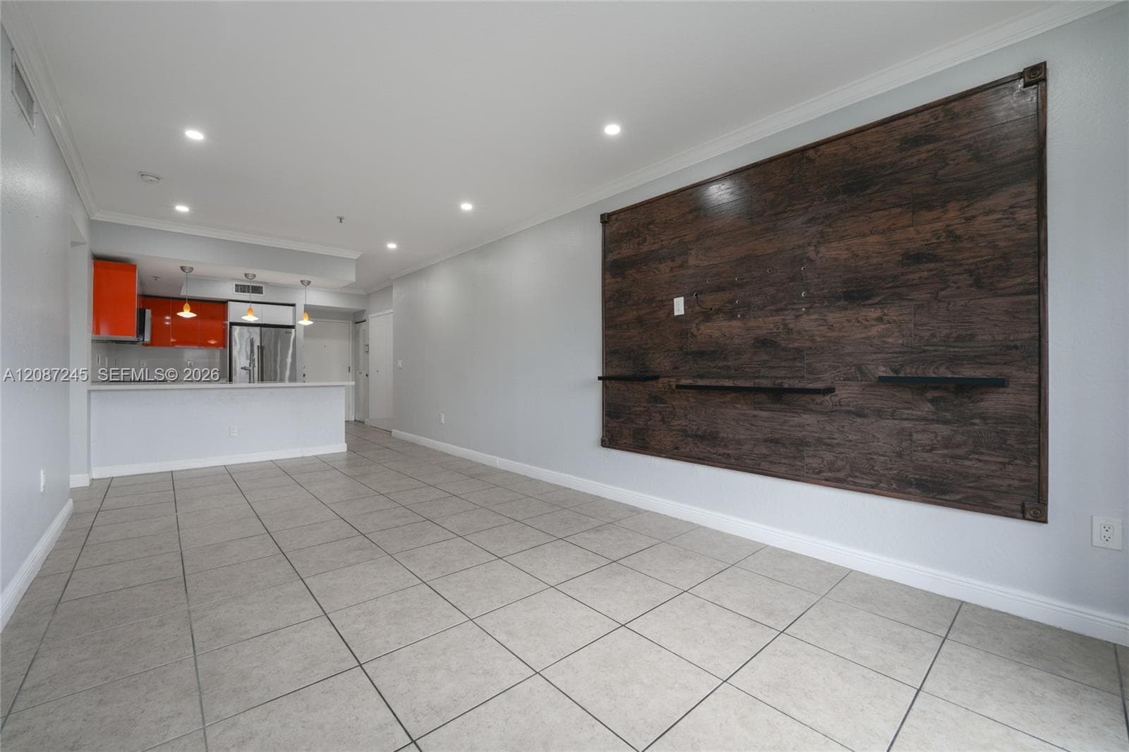 Open-concept interior featuring large-format tile flooring, a recessed wood-finish wall accent with integrated shelving, kitchen breakfast bar, and recessed lighting