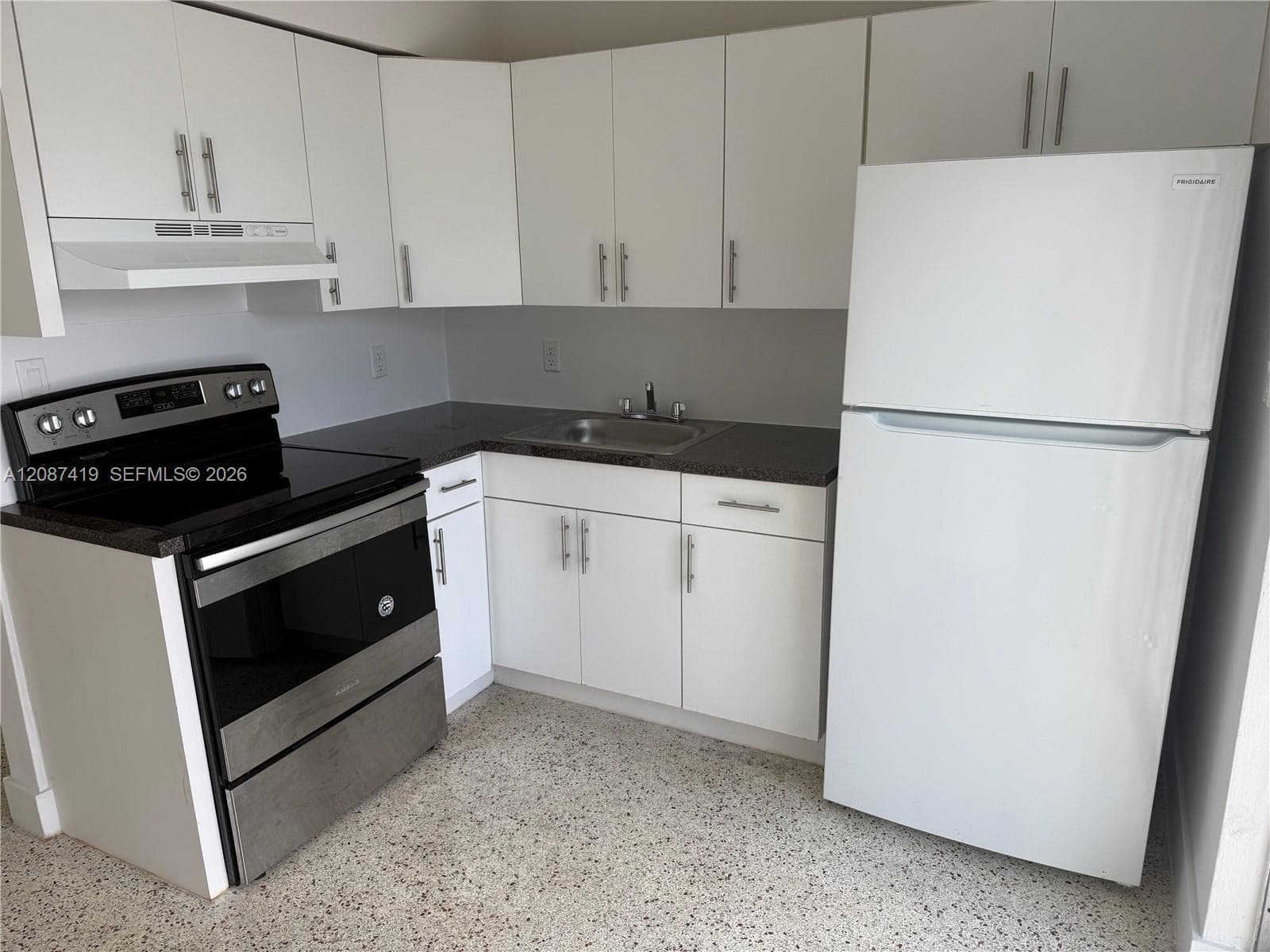 Kitchen featuring white shaker-style cabinetry, dark stone-finish countertops, stainless steel appliances, and terrazzo flooring