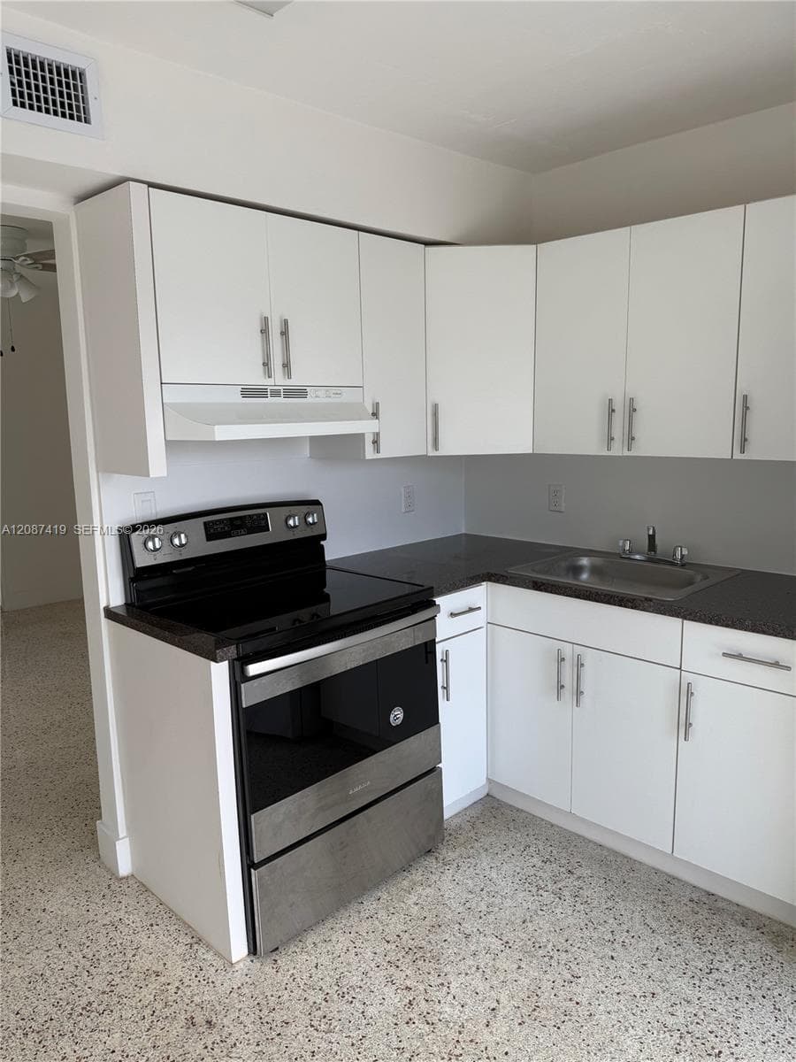 Kitchen featuring white shaker-style cabinetry, stainless steel range with overhead hood, dark countertops, and stainless steel undermount sink