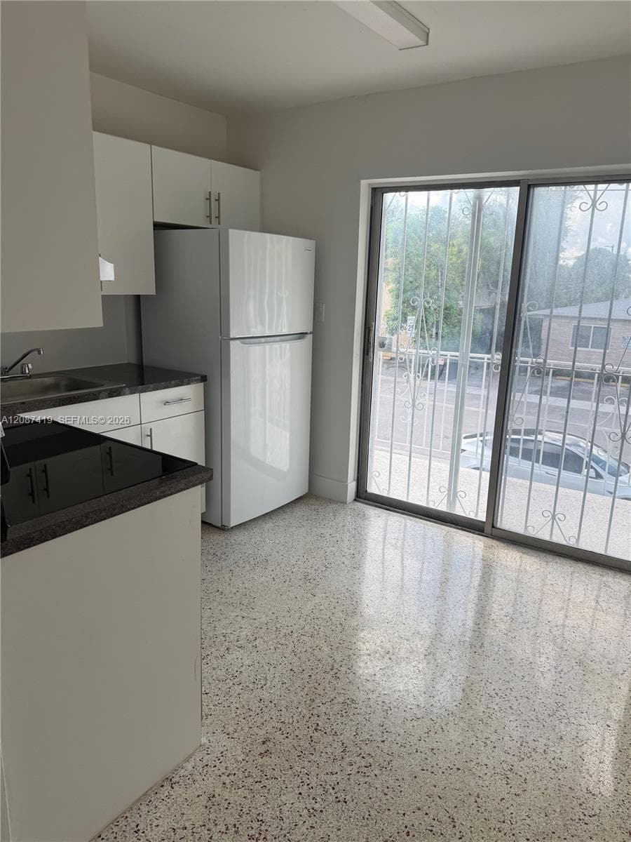 Kitchen area featuring white cabinetry, dark countertops, integrated white refrigerator, terrazzo flooring, and glass sliding doors