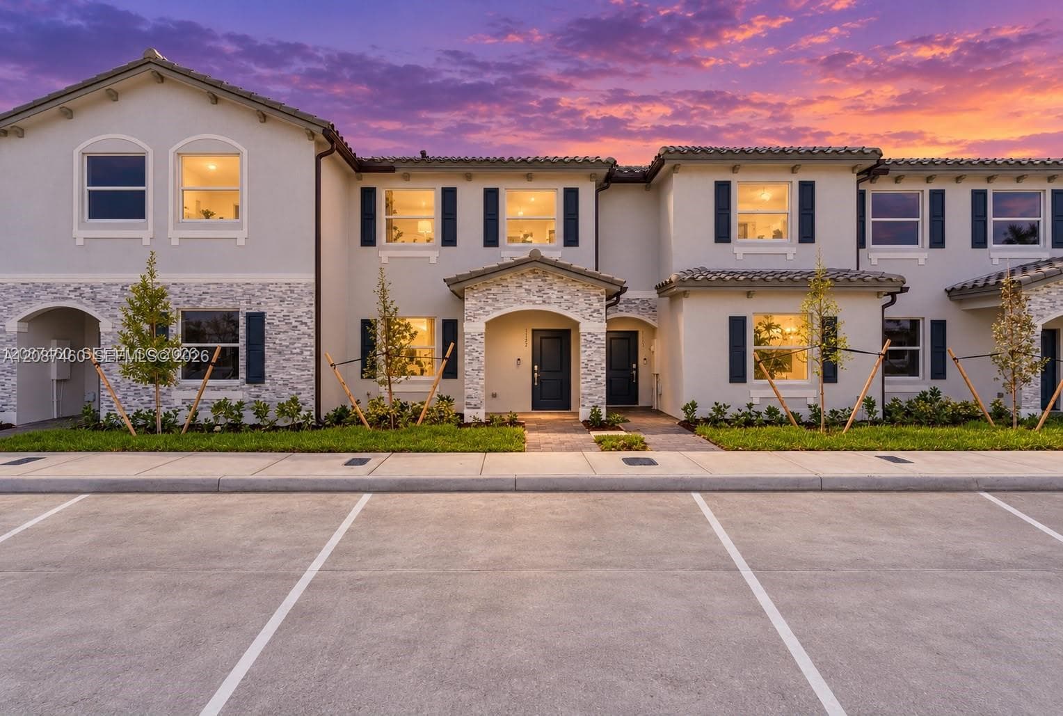 Stucco exterior featuring stacked stone veneer accents, tile roofing, dark paneled shutters, and covered portico entries