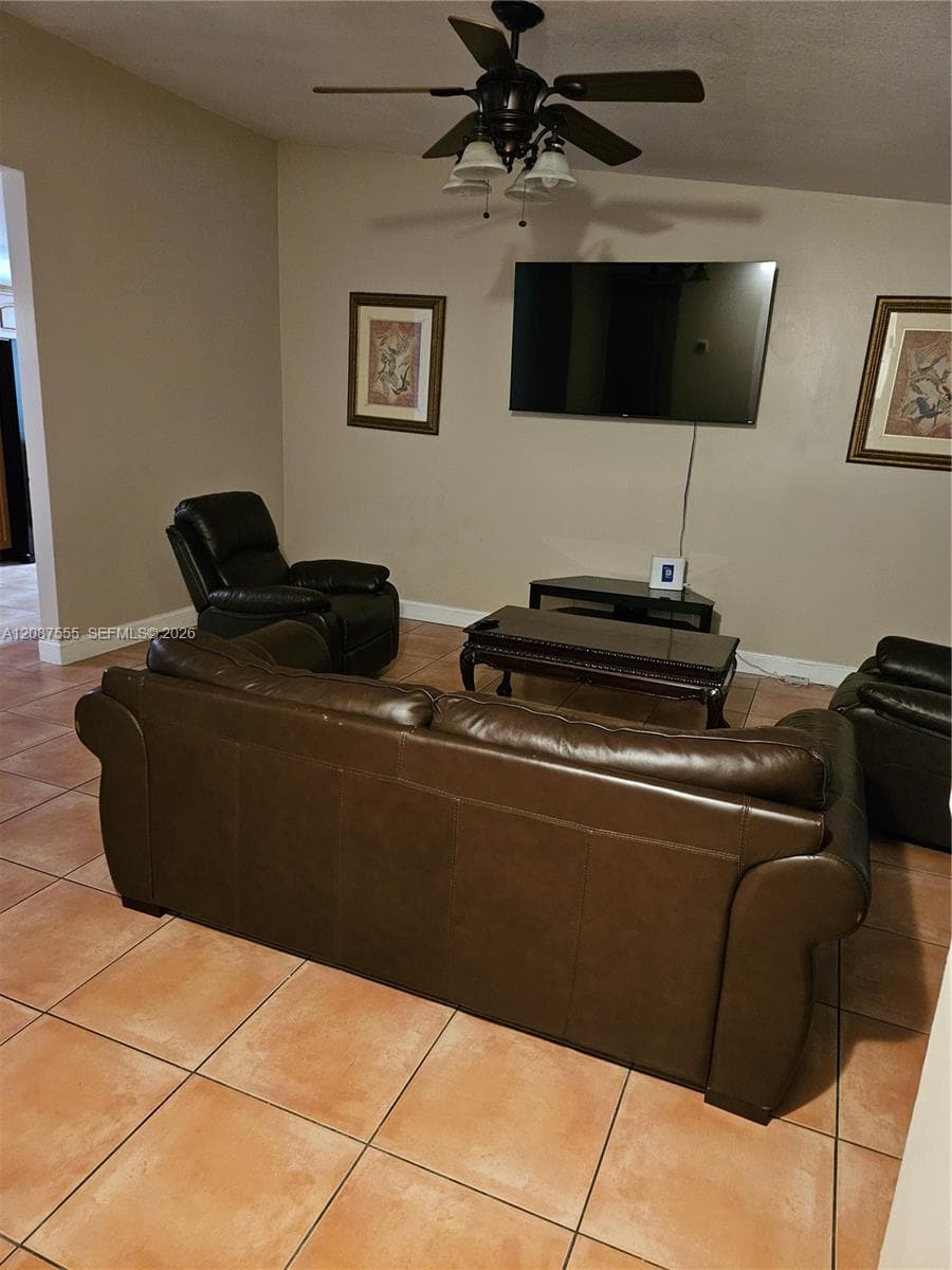 Living area featuring neutral wall paint, oversized ceramic tile flooring, and a ceiling fan with integrated light fixtures