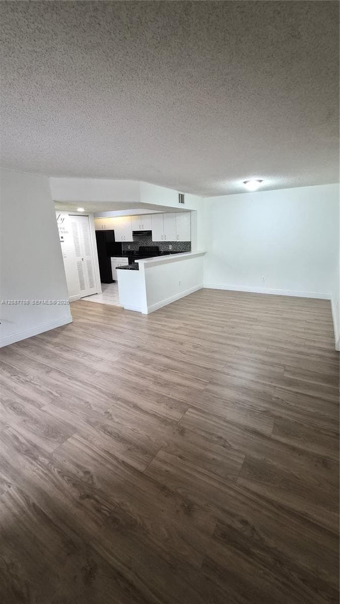 Open-concept living space featuring wood-finish flooring, white cabinetry, a breakfast bar, and flush-mount ceiling lighting
