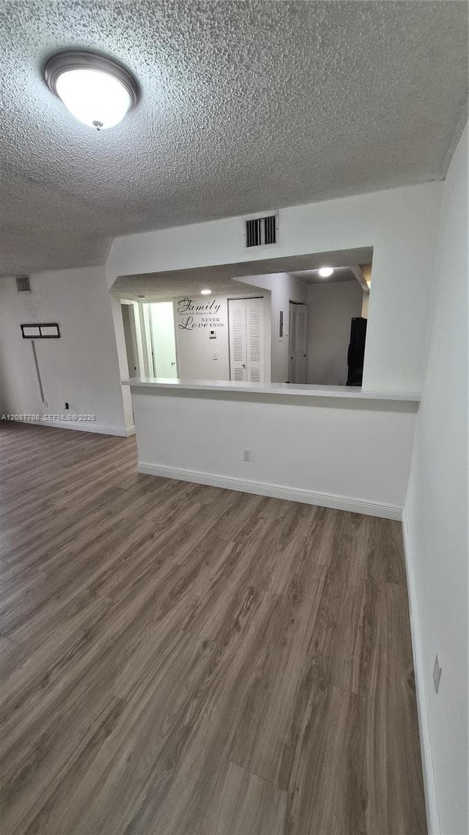 Interior space featuring wood-finish flooring, a pass-through opening with a flat-top counter, and a ceiling-mounted flush-mount light fixture