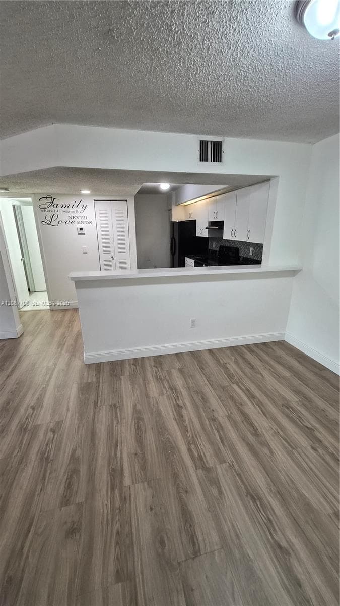 Open-concept floor plan featuring wood-finish flooring, white cabinetry, a built-in pass-through counter, and a closet with bifold doors