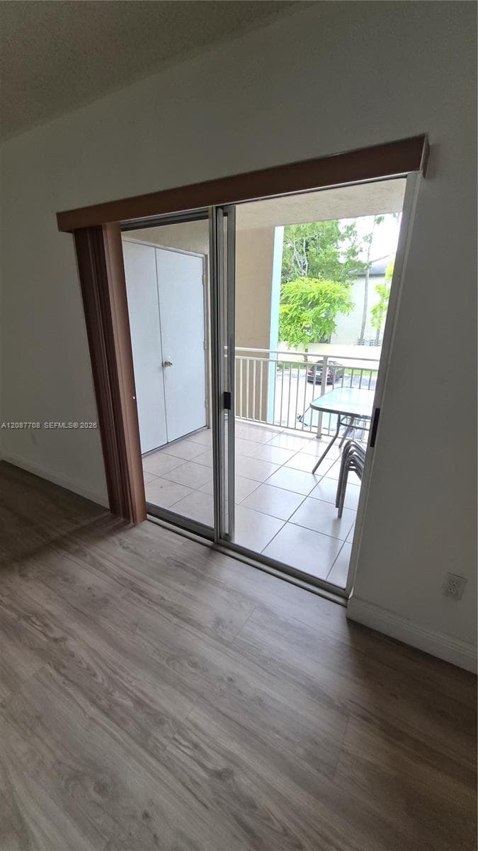 Sliding glass door with wood-finish trim, tile-floored balcony, metal railing, and integrated storage closet