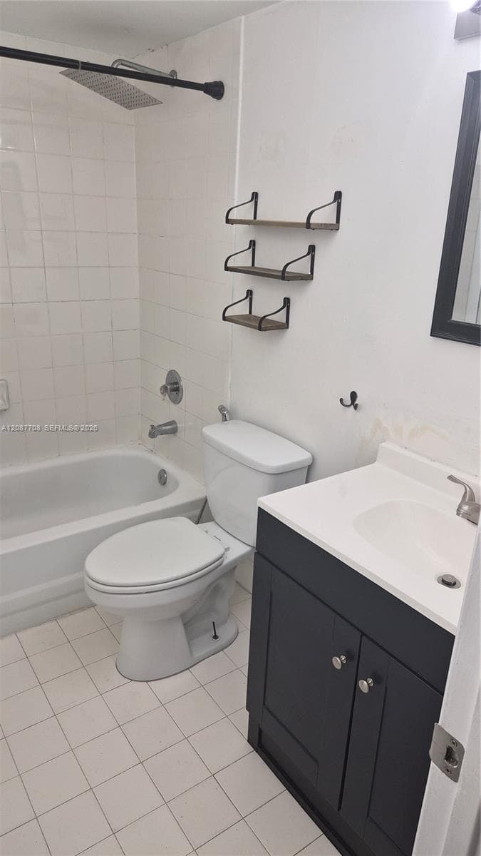 Bathroom featuring a square rainfall shower head, white ceramic tile tub surround, dark-finish vanity cabinet with a white countertop, and white tile flooring