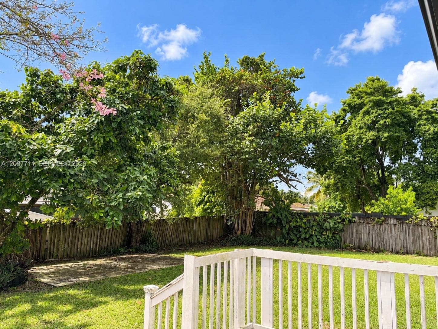Backyard featuring a wood deck with white railings, a concrete patio, perimeter wood fencing, and mature trees