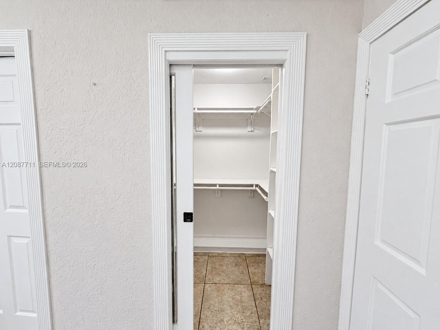 Walk-in closet featuring a sliding door, tiered white shelving, and tiled flooring