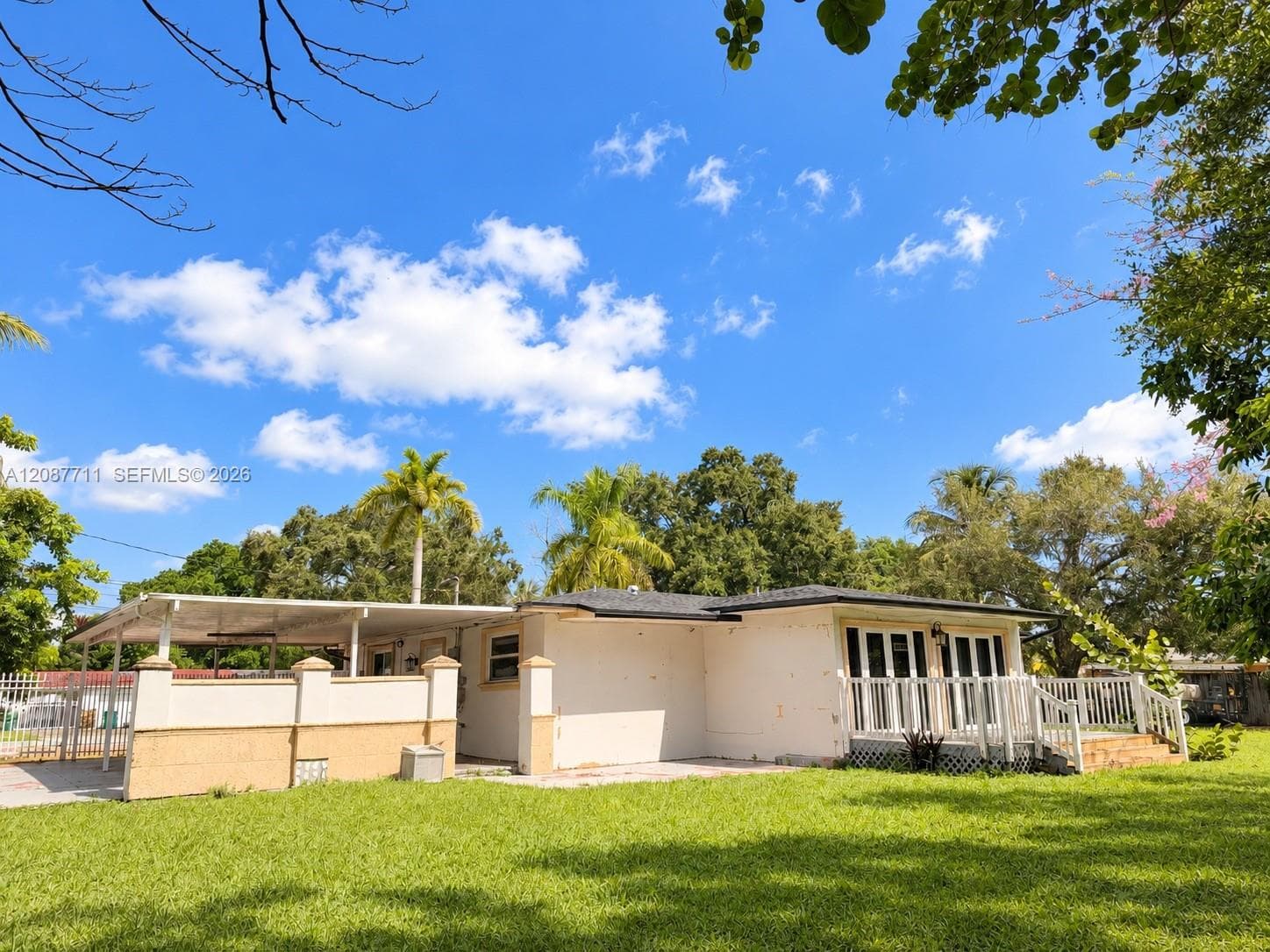 Single-story residence featuring an attached carport, covered side porch with decorative pillars, white railing, and a spacious lawn