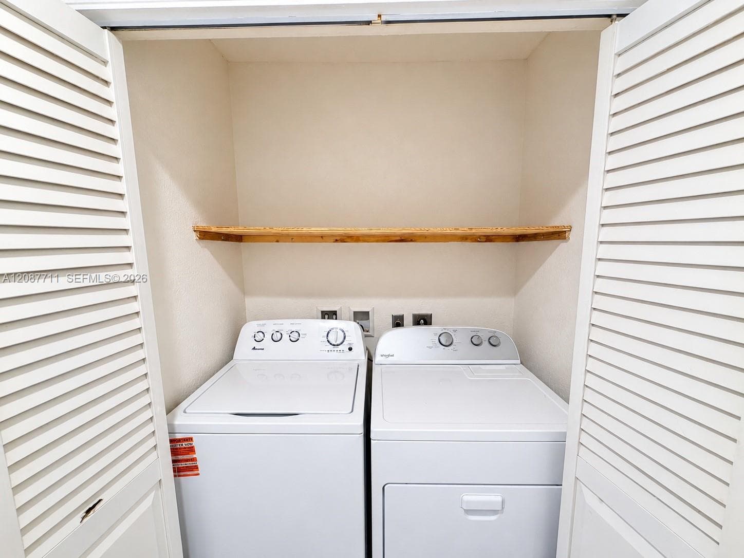 Laundry closet featuring white louvered doors and an installed wooden shelf