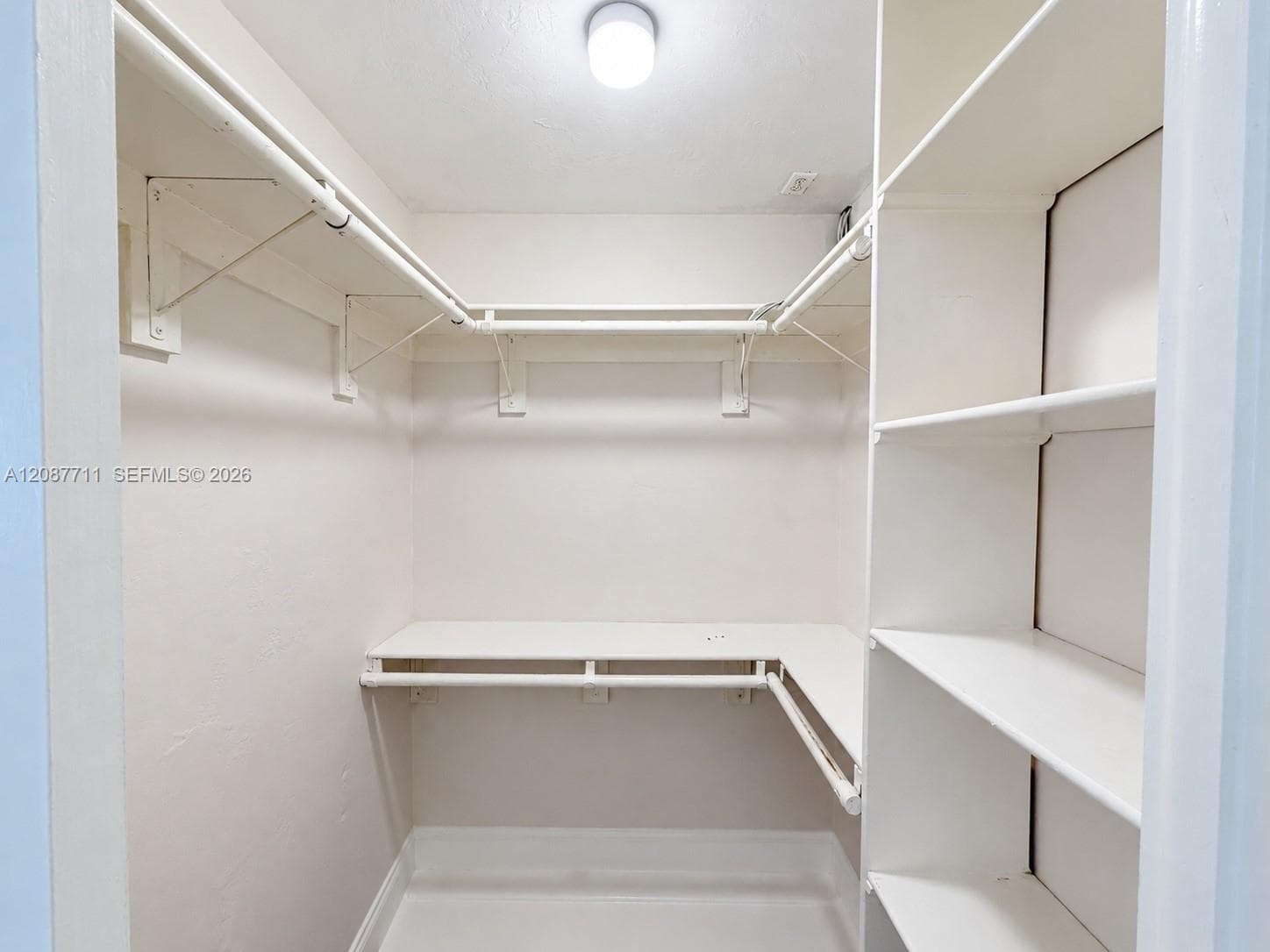 Walk-in closet featuring tiered wrap-around metal garment rods and custom built-in white shelving