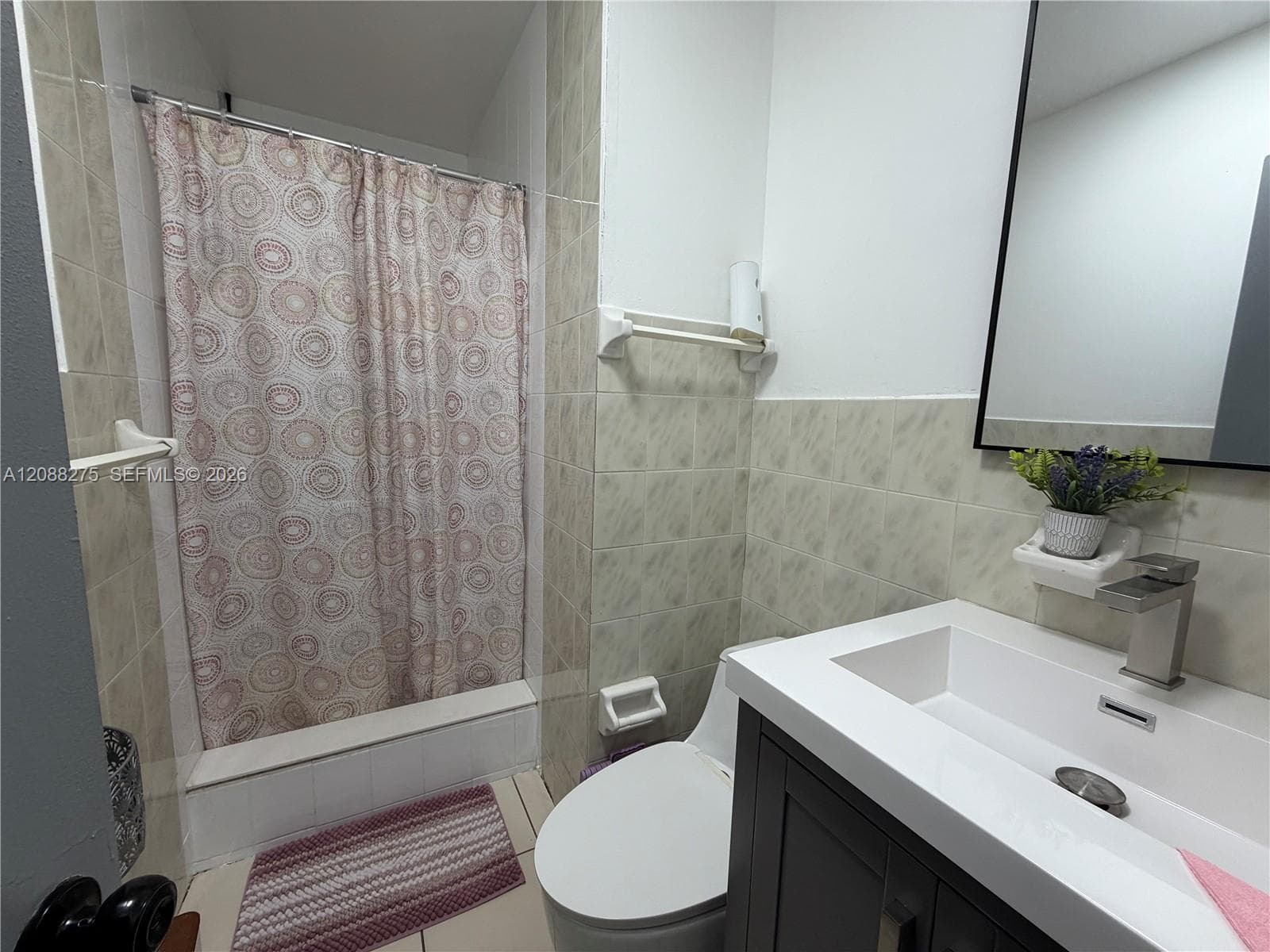 Modern vanity with an integrated rectangular sink and metallic faucet, dark-toned cabinetry, light-toned wall tile surround, and a tub-shower combination