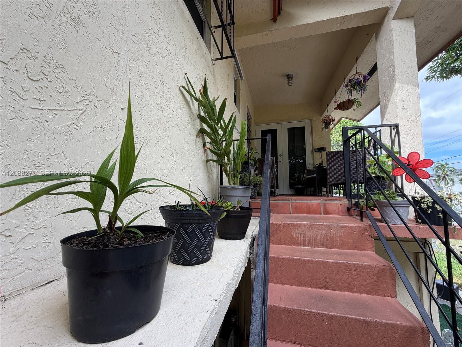 Covered front porch featuring terracotta-tiled steps, wrought-iron handrails, a stucco exterior finish, and double-entry doors