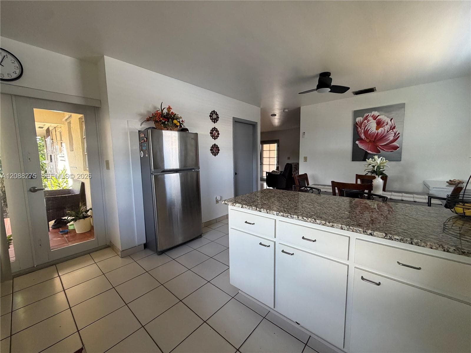 Kitchen featuring a stone-topped central island, white cabinetry, tile flooring, stainless steel refrigerator, and ceiling fan