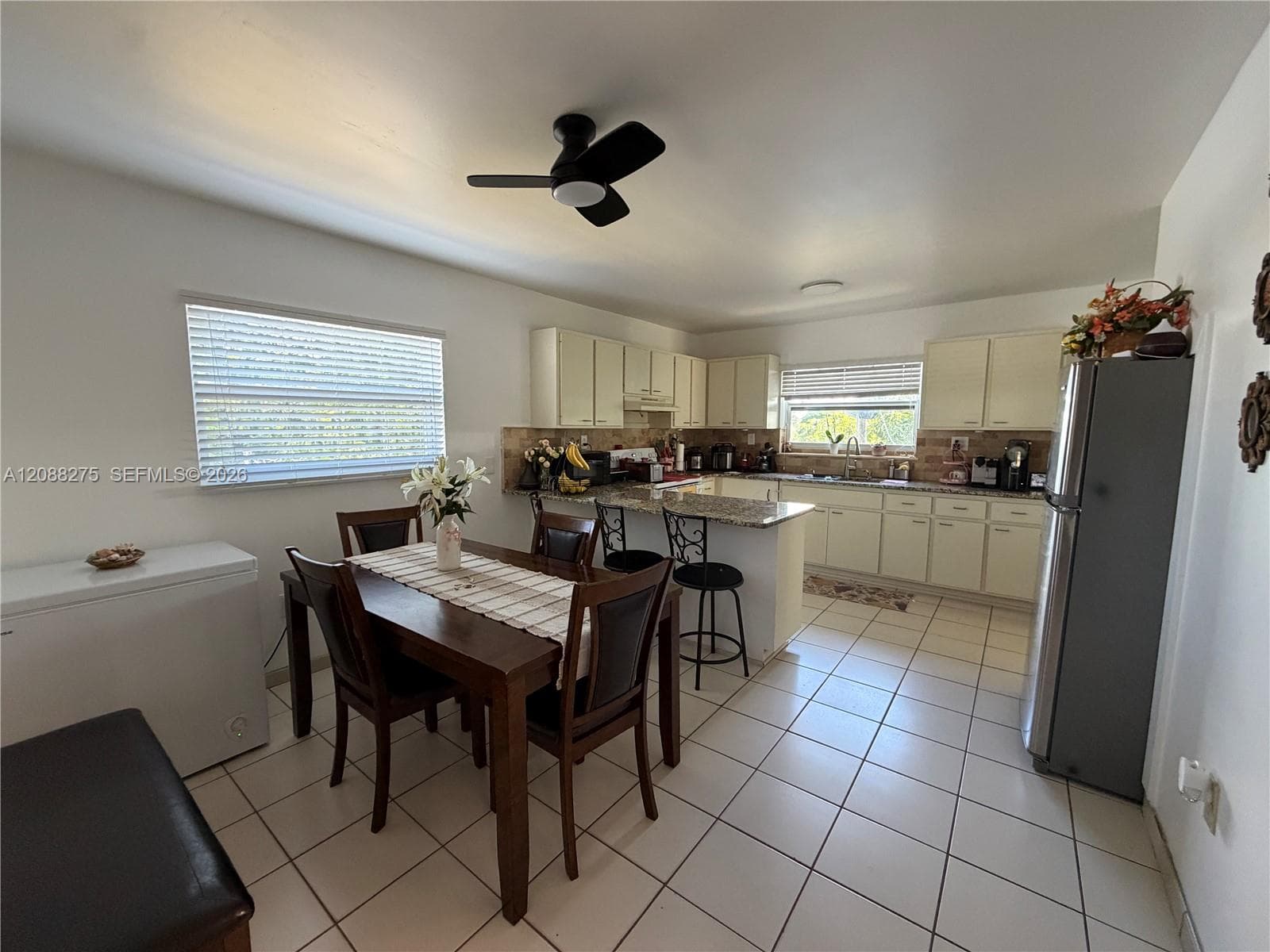 Kitchen featuring tile flooring, light-toned cabinetry, stone-finish countertops, a dual-basin stainless steel sink, and a ceiling-mounted fan