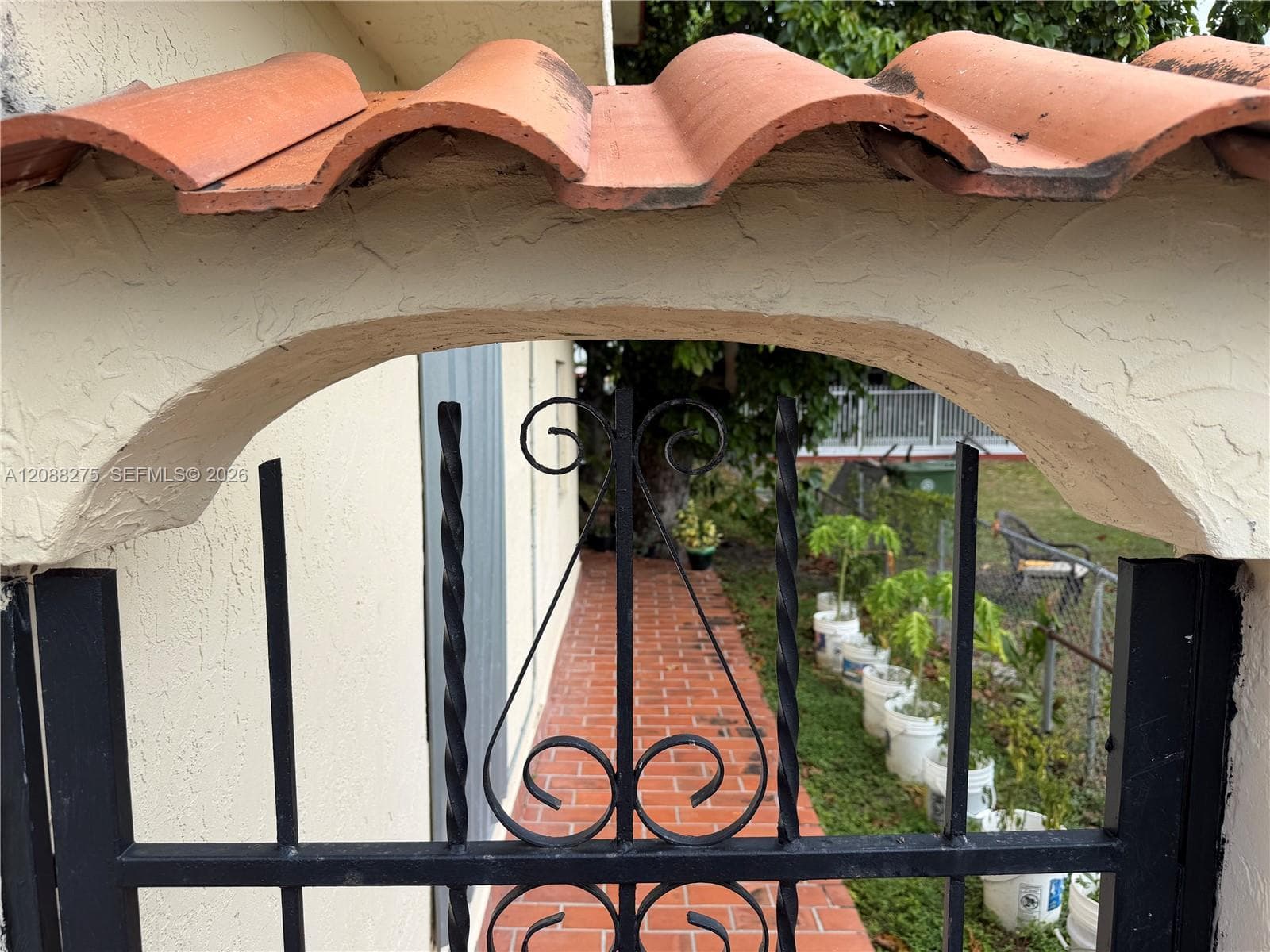 Exterior entry featuring a terracotta tiled roof arch, textured stucco finish, and a black wrought-iron gate with decorative scrollwork