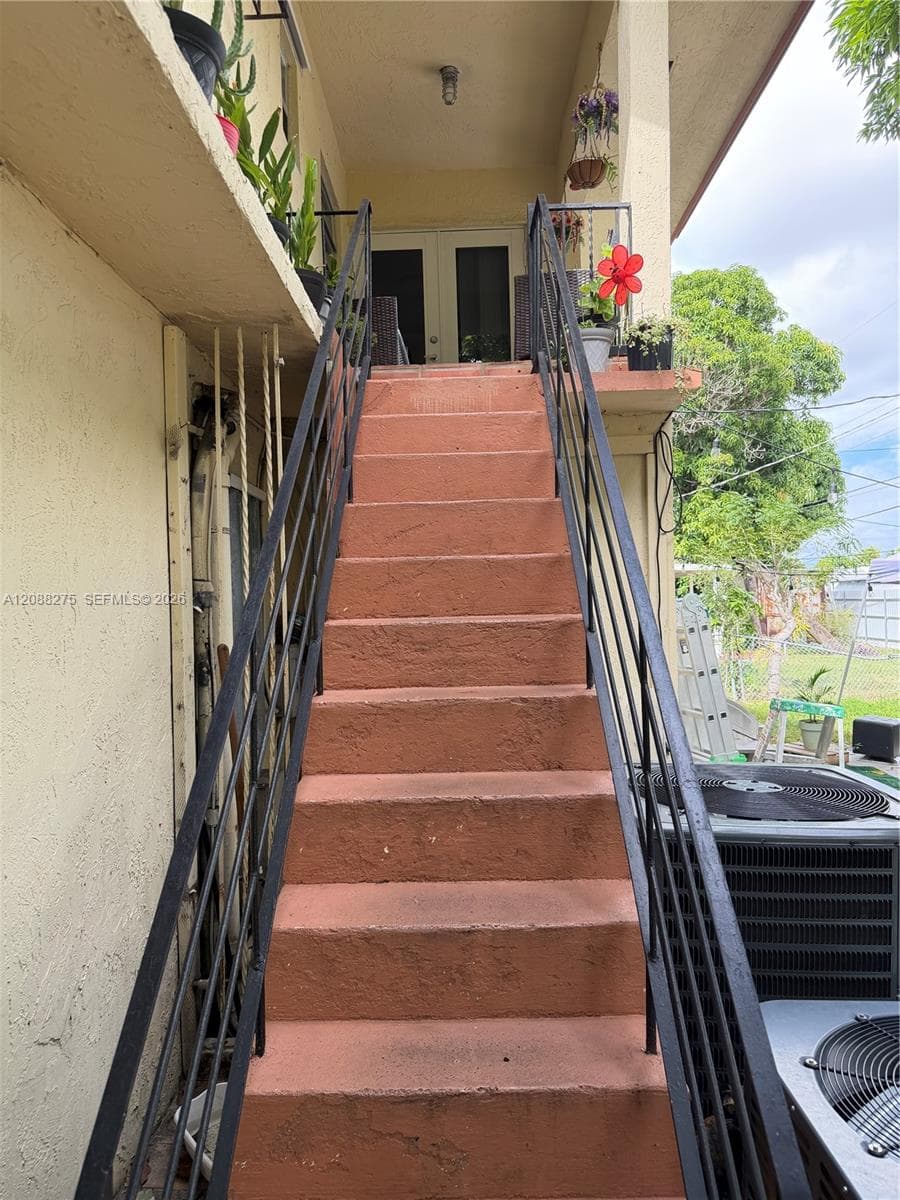 Exterior staircase with textured concrete steps and black metal railings leading to a landing with dual glass-panel entry doors