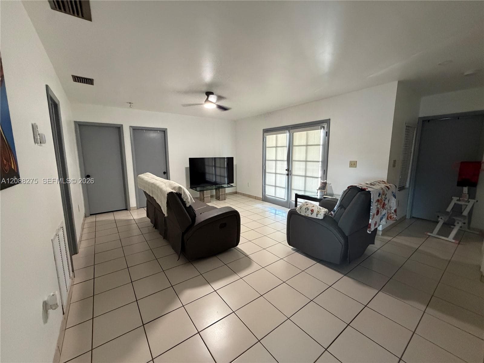 Spacious room featuring neutral ceramic tile flooring, a ceiling fan with integrated lighting, and glass-paned double doors