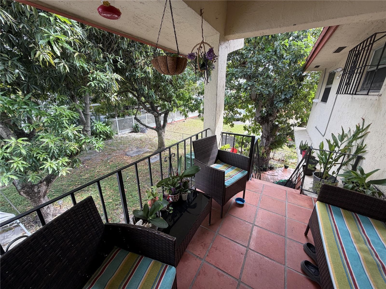 Covered balcony featuring terracotta-style tile flooring, black metal railing, and mature landscaping