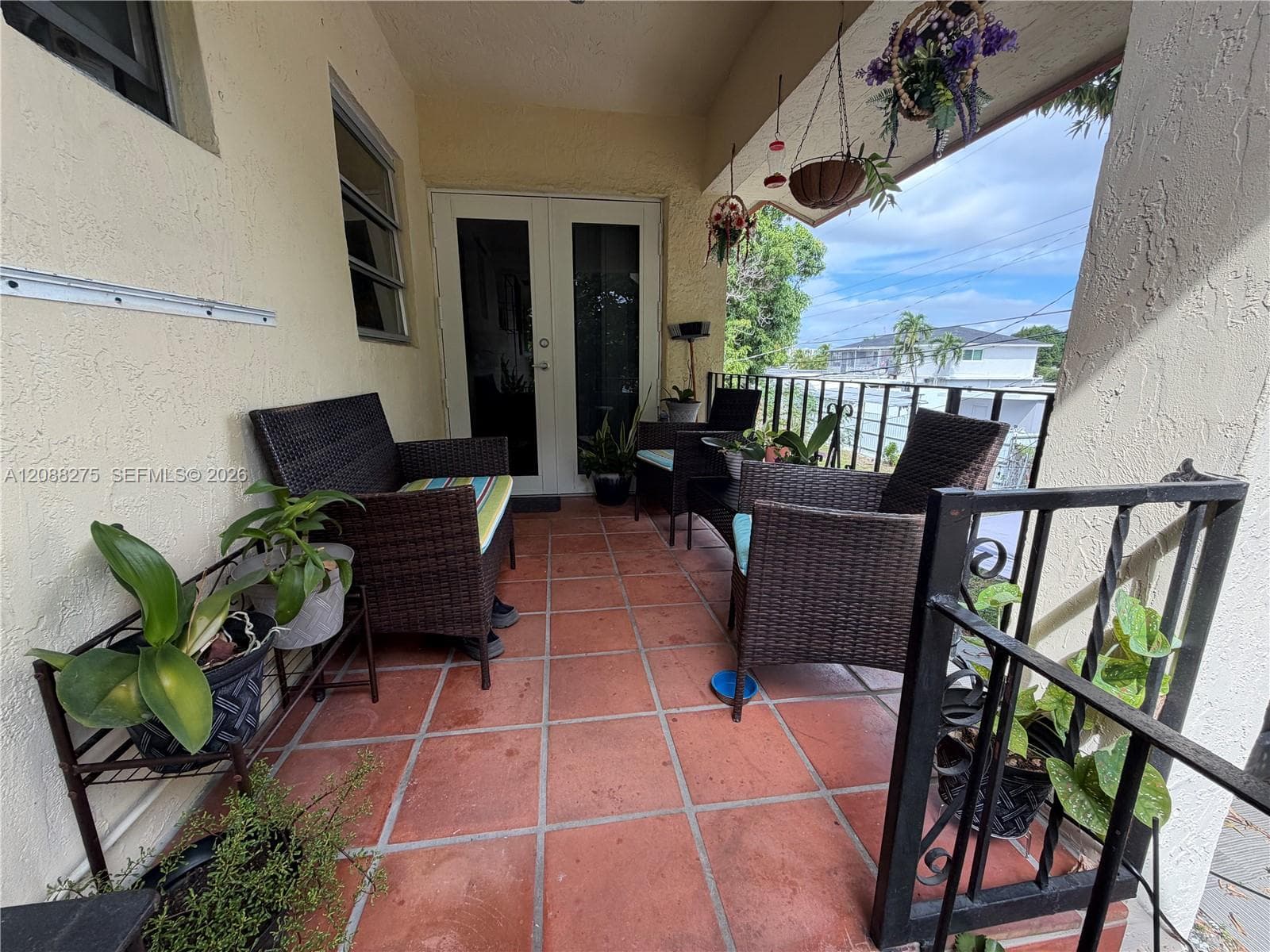 Covered exterior porch featuring terracotta tile flooring, wrought iron railings, and double-glass entry doors