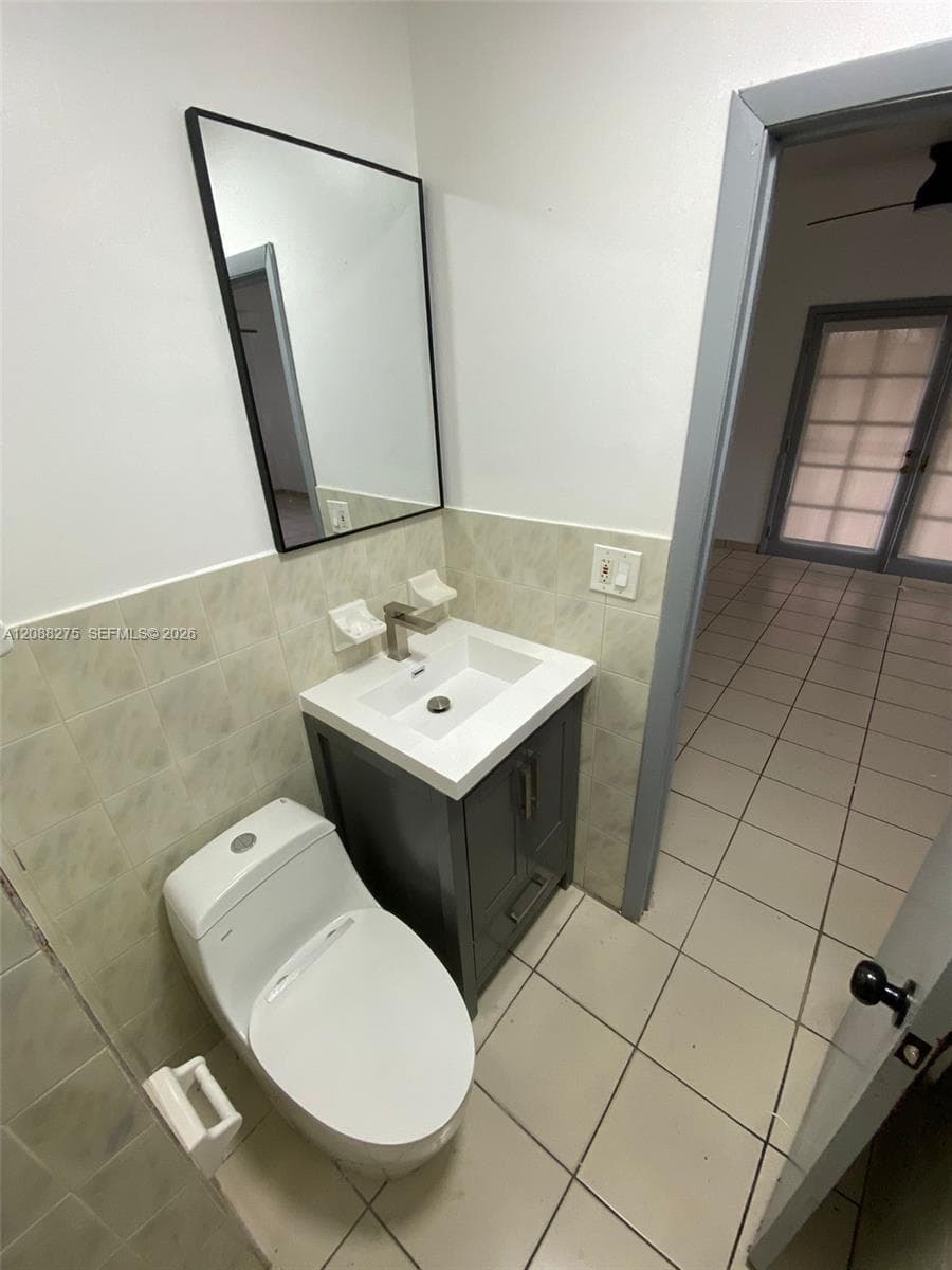 Bathroom featuring a vanity with a white rectangular sink, matte metallic faucet, and dark-toned cabinetry, complemented by a rectangular wall-mounted mirror with a black frame and light-toned wall tile
