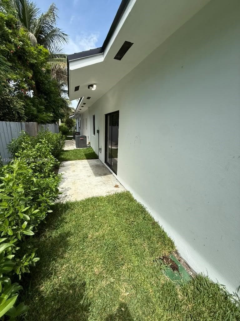 Exterior side yard featuring a concrete patio, green space, recessed soffit lighting, and perimeter shrubbery