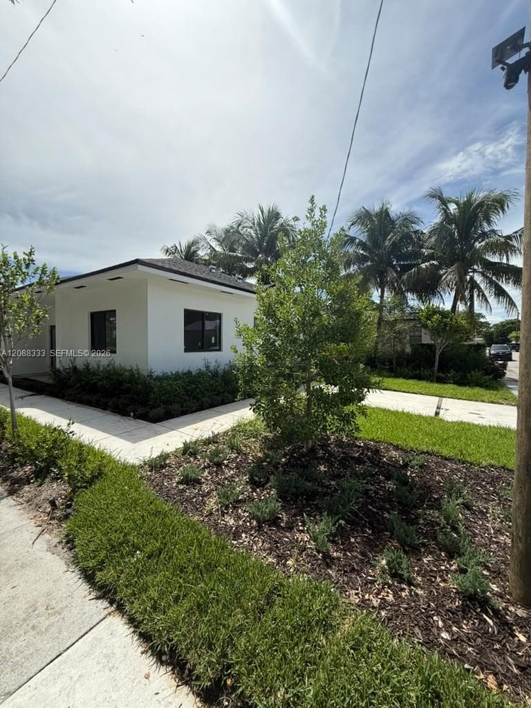 Exterior featuring smooth white stucco finish, dark-trimmed windows, concrete walkway, and landscaped garden beds with mature palms