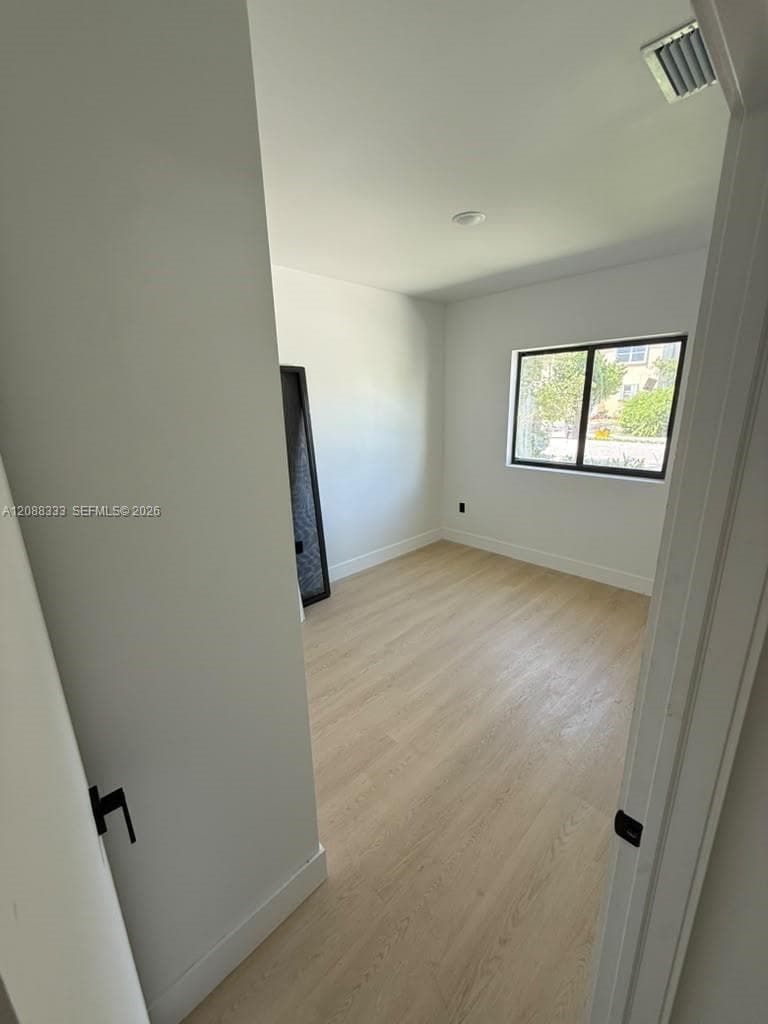 Interior space featuring wood-finish flooring, white walls, and a single-pane window with a black frame