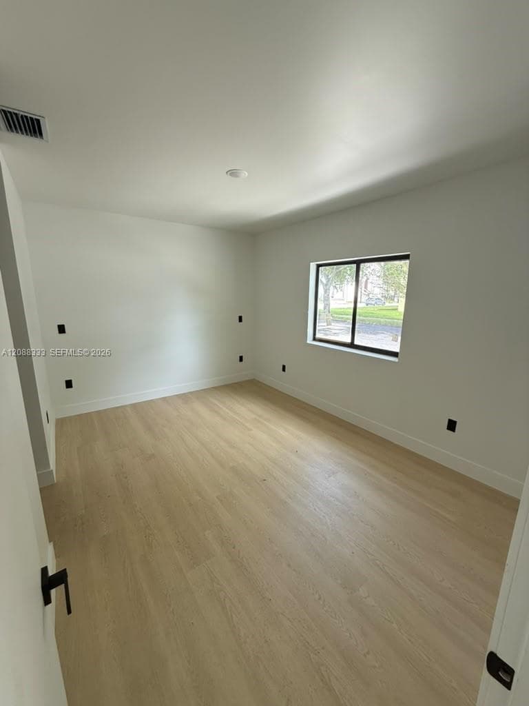 Room featuring wood-finish flooring, crisp white walls, a single-pane window with a black frame, and matte black electrical outlets