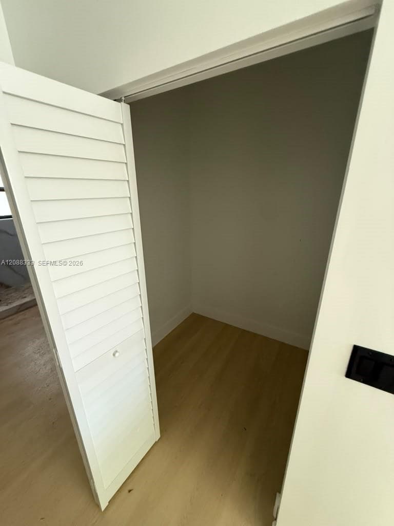Storage space featuring white louvered bifold doors and wood-finish flooring
