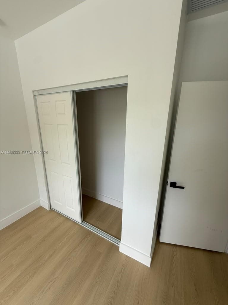 Wood-finish flooring throughout, closet with paneled sliding doors, and interior door featuring matte black hardware