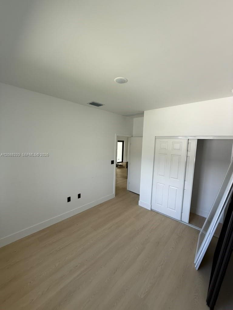 Interior space featuring wood-finish flooring, white walls, and a closet with sliding panel doors