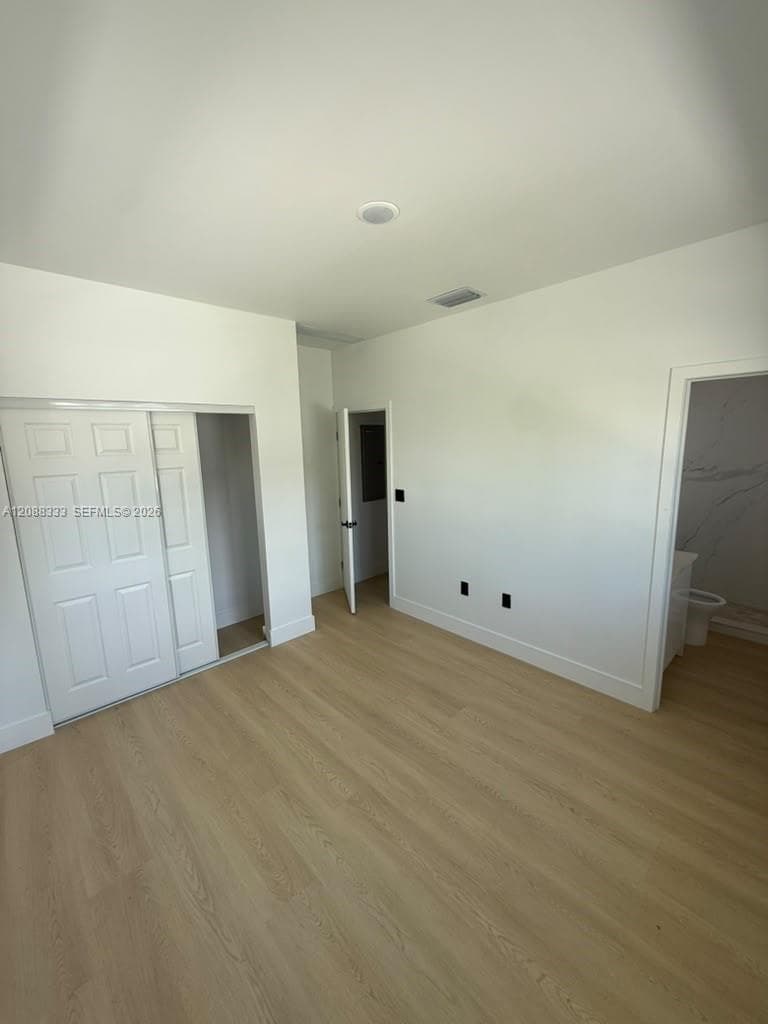 Neutral interior space featuring wood-finish flooring, crisp white walls, and a multi-panel sliding closet door