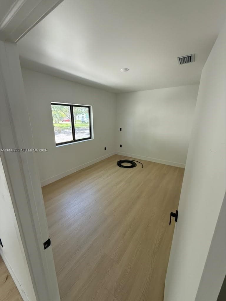 Interior space featuring neutral wall paint, wood-finish flooring, and a single-pane window with a black frame