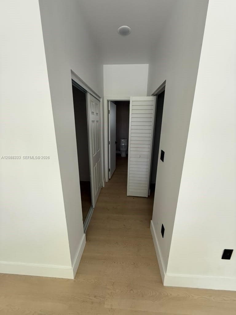 Hallway featuring wood-finish flooring, two-panel interior doors, and white louvered closet doors