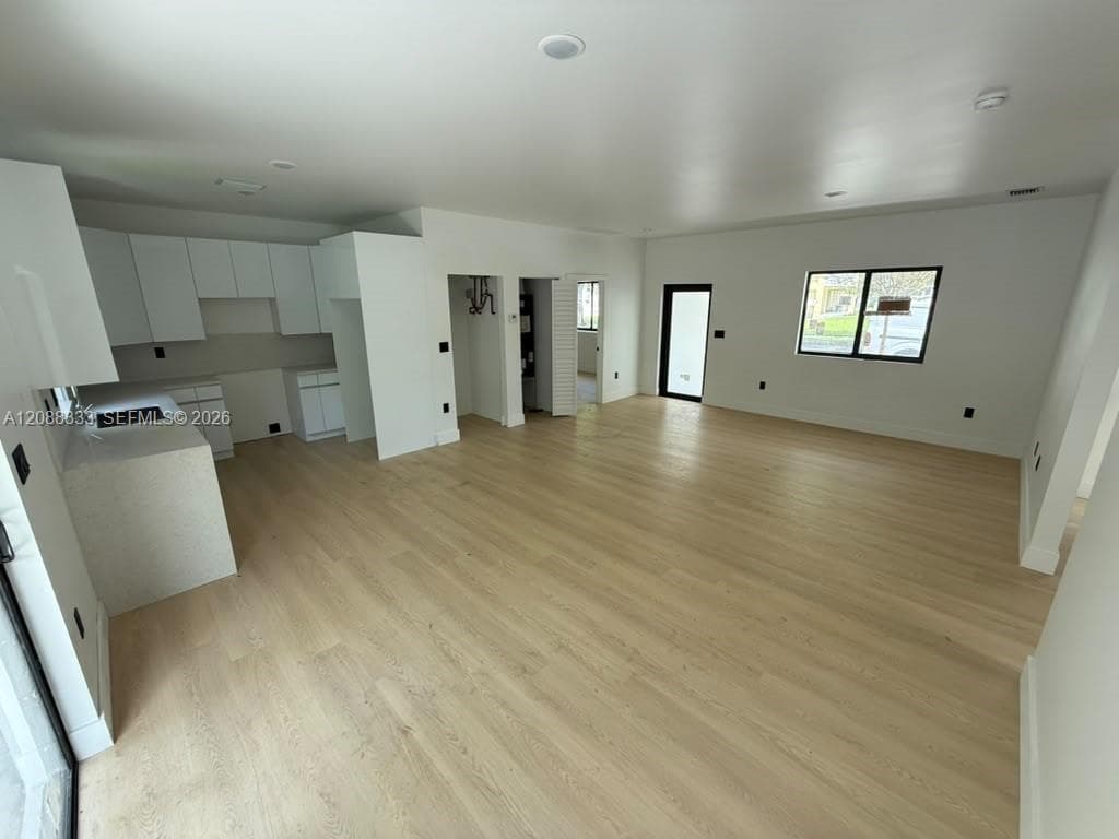Open-concept interior featuring light-toned wood-finish flooring, white flat-panel cabinetry, stone-finish countertops, and black window and door frames