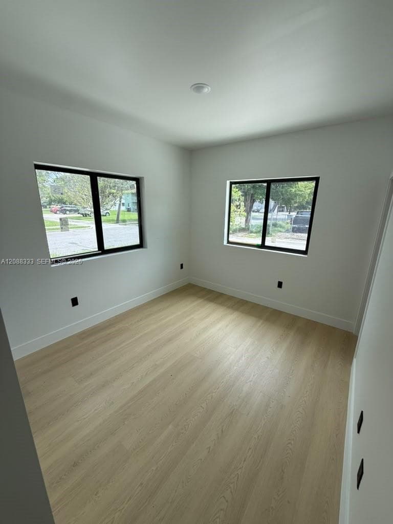 Neutral room featuring wood-finish flooring, crisp white walls, and black-framed windows