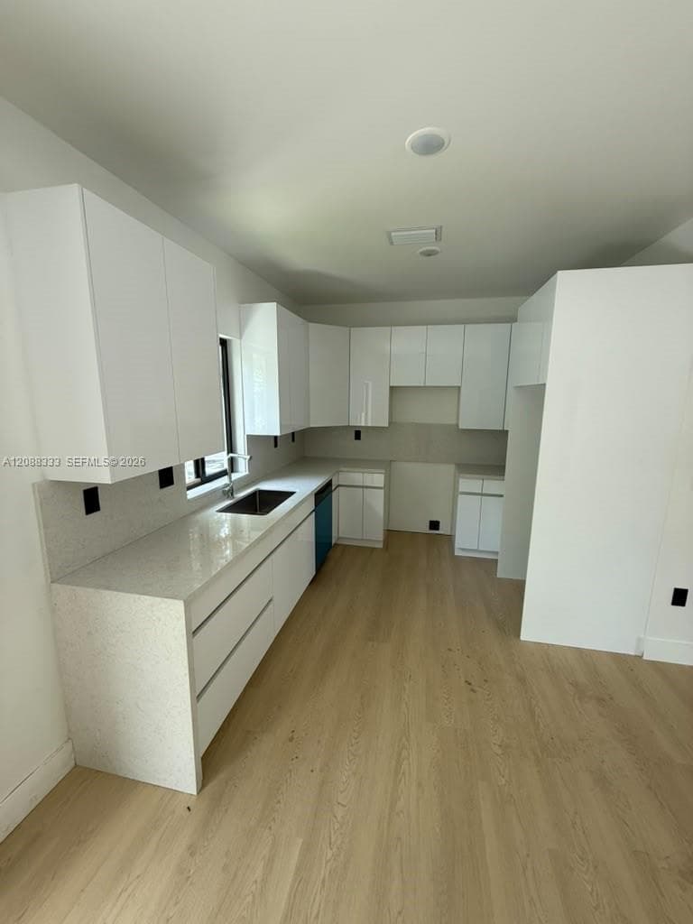 Kitchen featuring flat-panel white cabinetry, light-toned stone-finish countertops, wood-finish flooring, and an undermount stainless steel sink