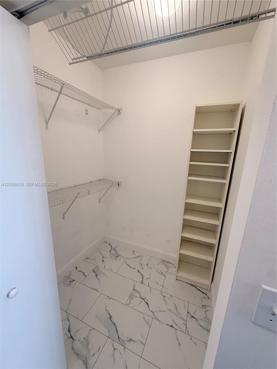 Storage space featuring tile flooring with a marble-patterned finish, multi-level wire shelving, and built-in vertical shelving unit
