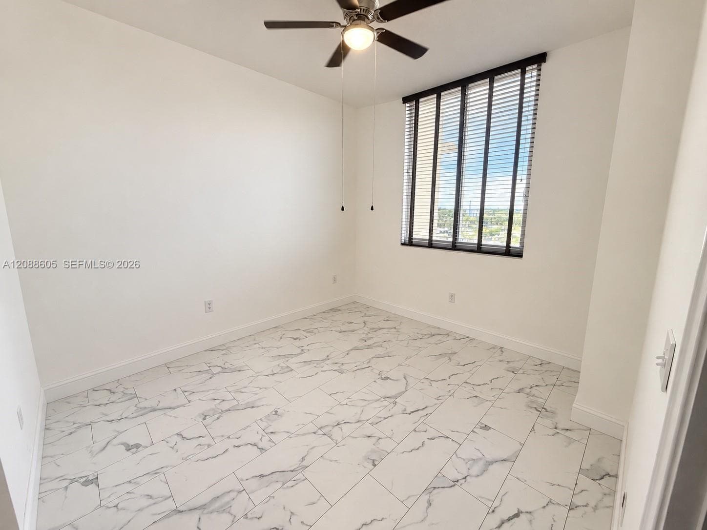 Room featuring large-format tile flooring with a veined pattern, floor-to-ceiling style windows with integrated blinds, and a ceiling fan with integrated lighting