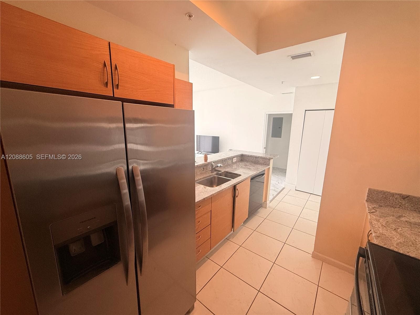 Kitchen featuring stainless steel appliances, wood-finish cabinetry, stone-style countertops, double-basin sink, and tile flooring