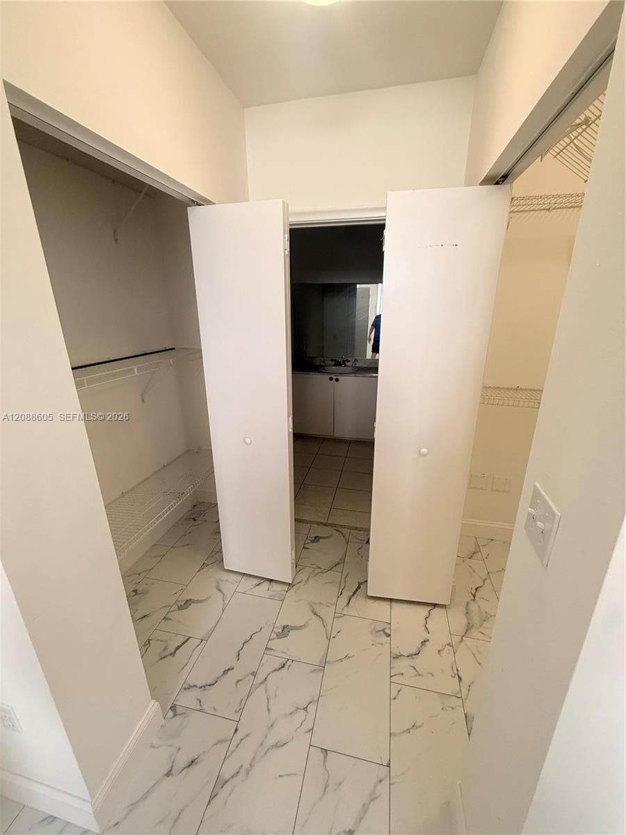 Walk-in closet featuring large-format tile flooring with a veined pattern, dual bifod doors, and installed wire shelving