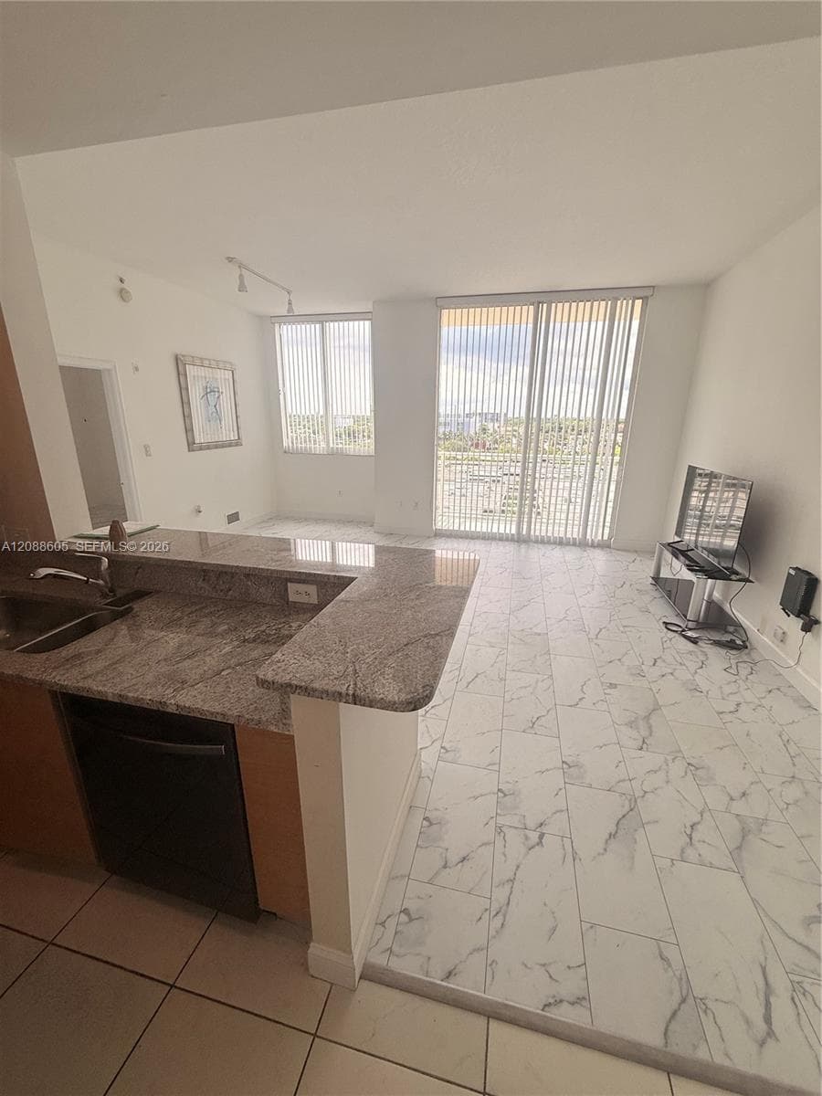 Kitchen featuring stone-finish countertops, stainless steel sink with metal faucet, floor-to-ceiling windows, and tile flooring with a veined pattern