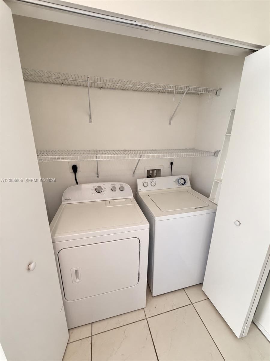 Laundry closet featuring built-in dual-tier wire shelving, tile flooring, and dedicated hookups for a washer and dryer