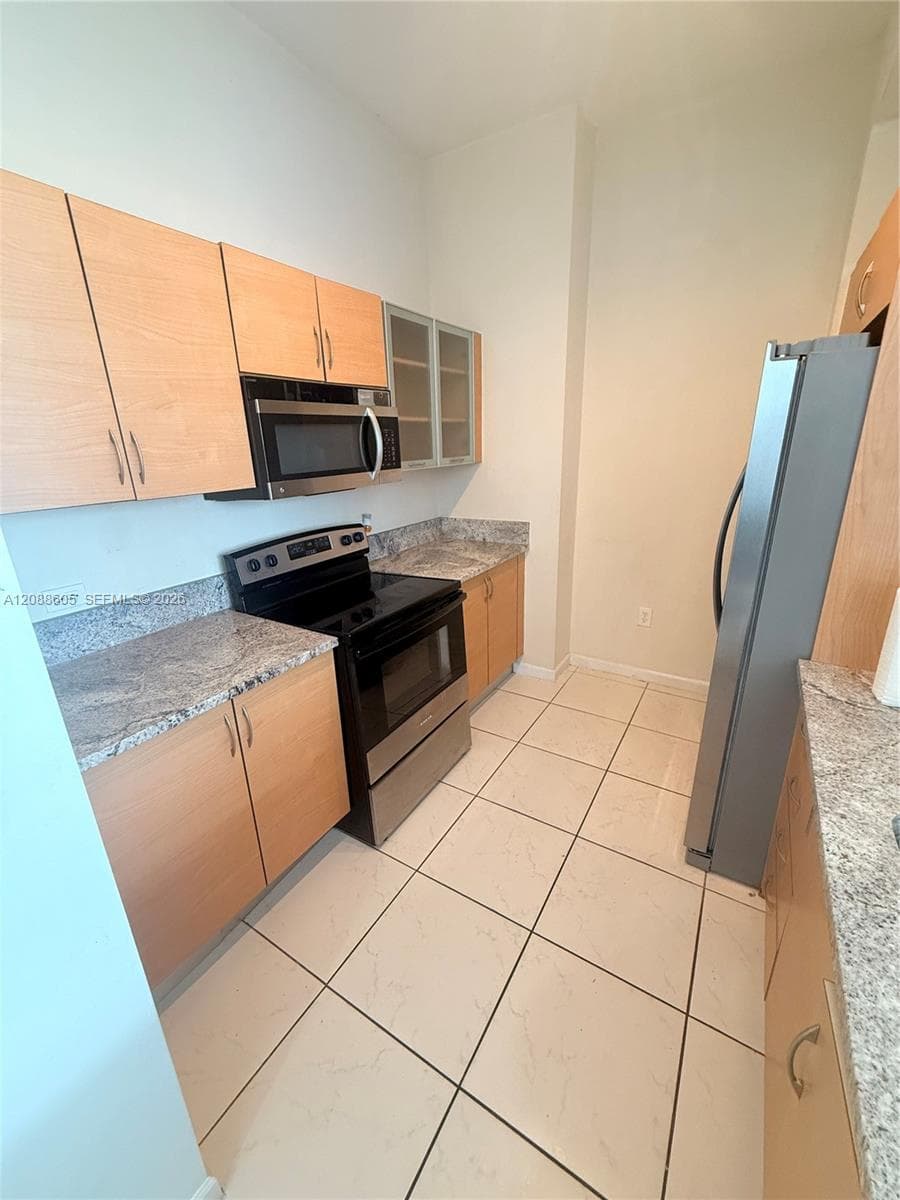 Kitchen featuring light-finish cabinetry, stone-patterned countertops, stainless steel appliances, and tile flooring