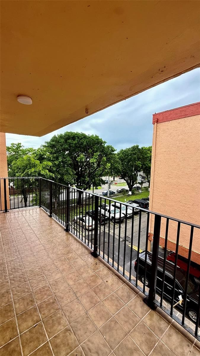 Covered balcony featuring square-tile flooring and black metal railing