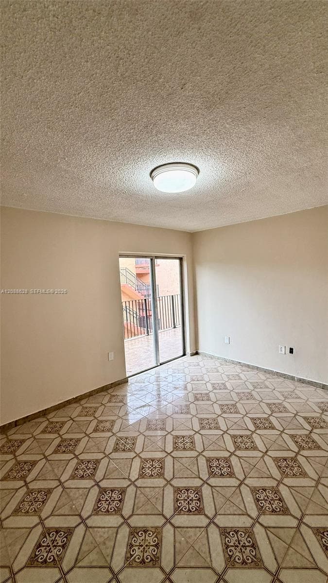 Neutral-toned walls, geometric patterned tile flooring, textured ceiling, flush-mount light fixture, and sliding glass door leading to an exterior balcony