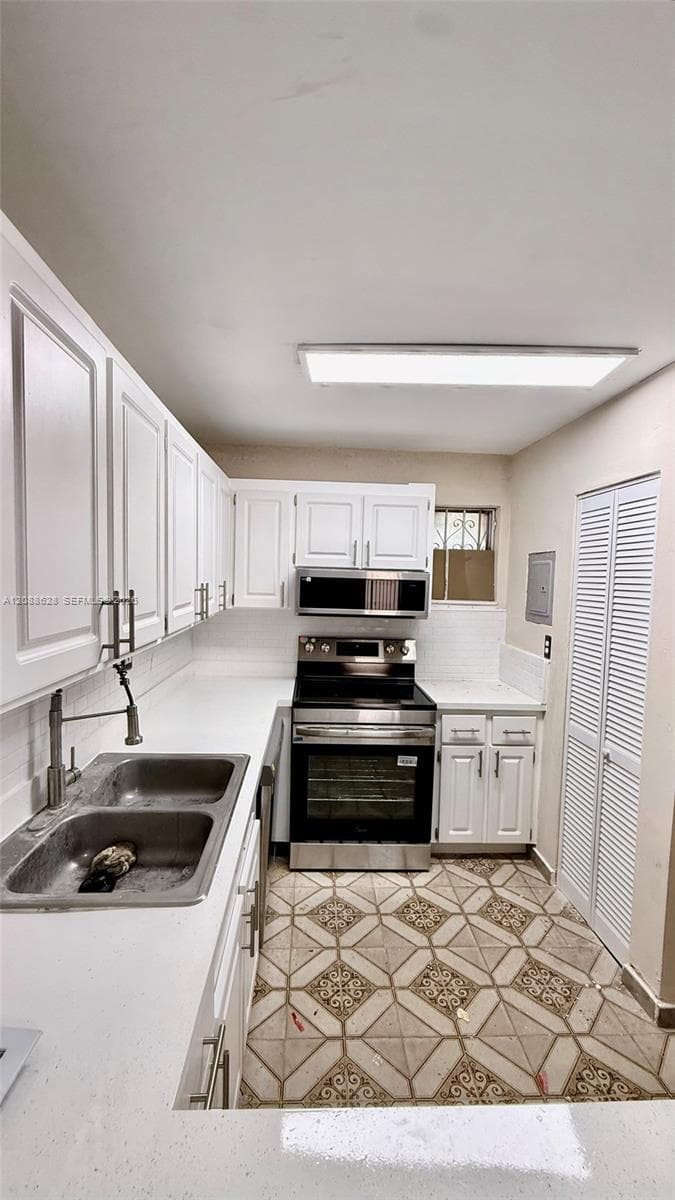 Kitchen featuring white cabinetry, stainless steel appliances, double-basin undermount sink with a gooseneck faucet, patterned tile flooring, and bi-fold louvered closet doors